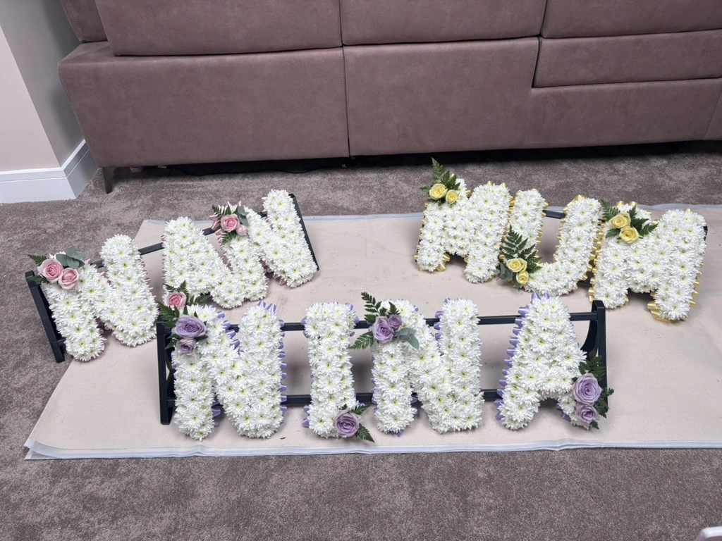 Fresh flower-word tributes spelling NAN, MUM, and NINA in white chrysanthemums