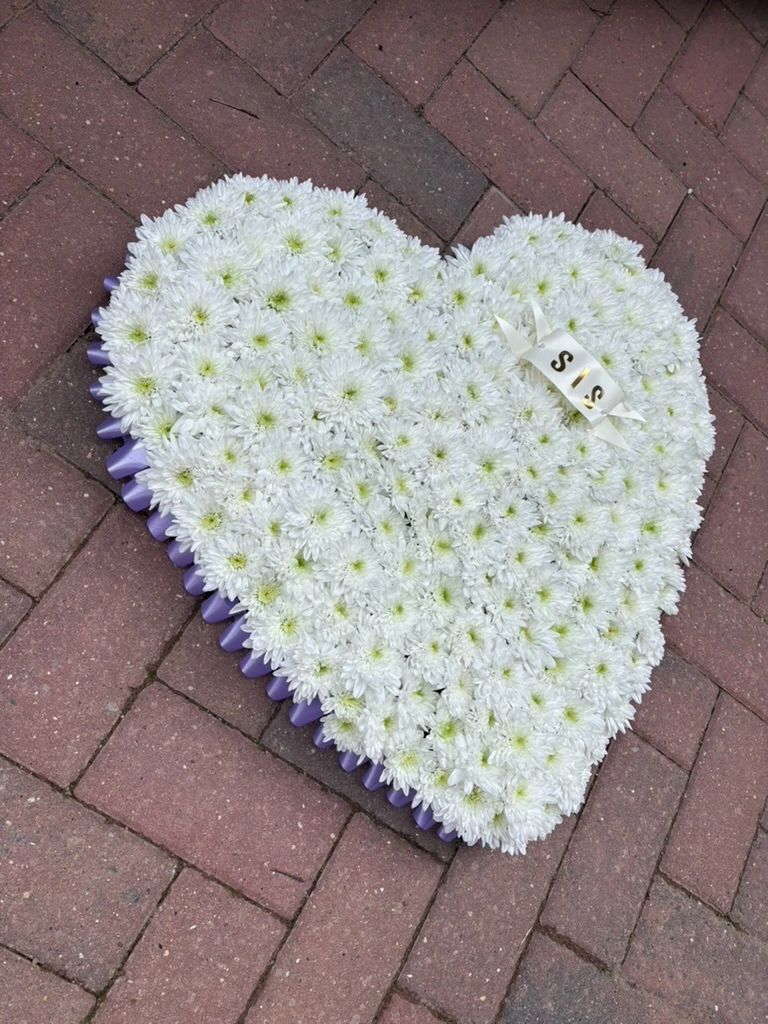 A fresh heart tribute massed in white chrysanthemums with a lilac cellophane edge and a personalised Sis name ribbon